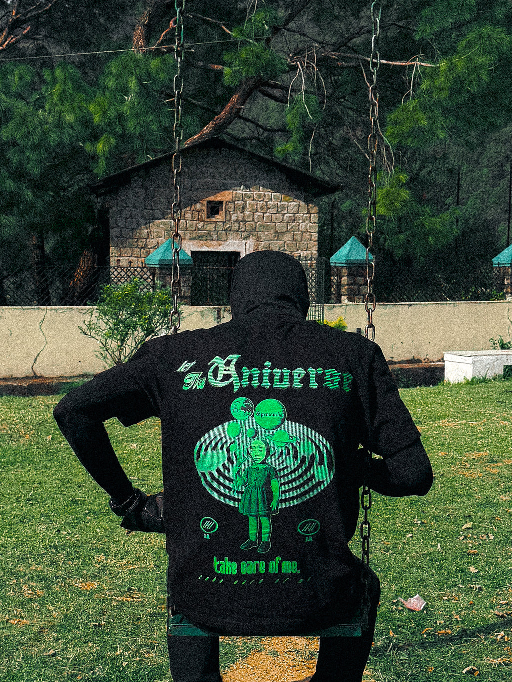 Person wearing a black hoodie with green graphics and text in an outdoor setting.