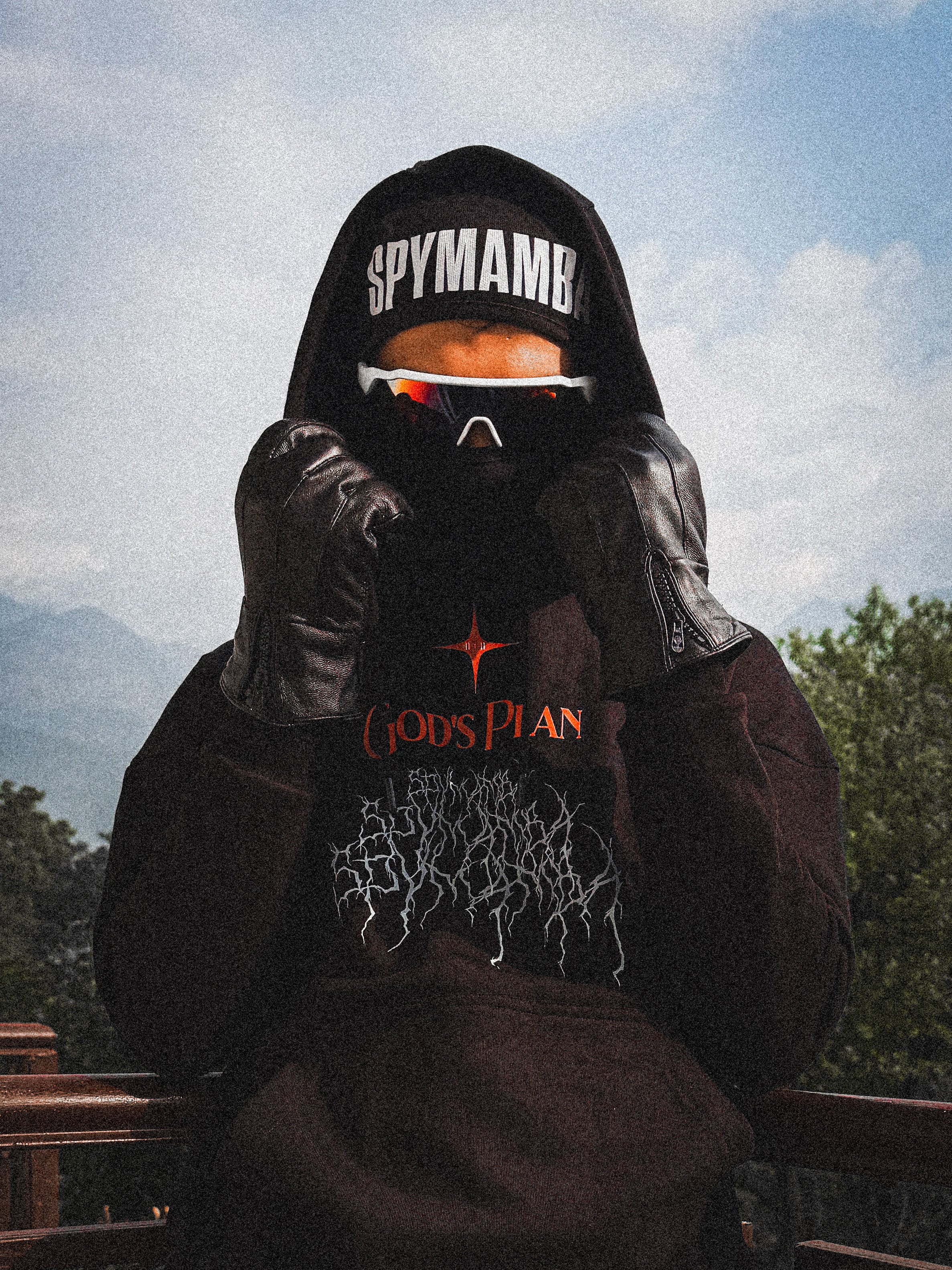 Person wearing a hoodie with 'Spyman' text and a t-shirt with 'Gods Plan' text, outdoors.